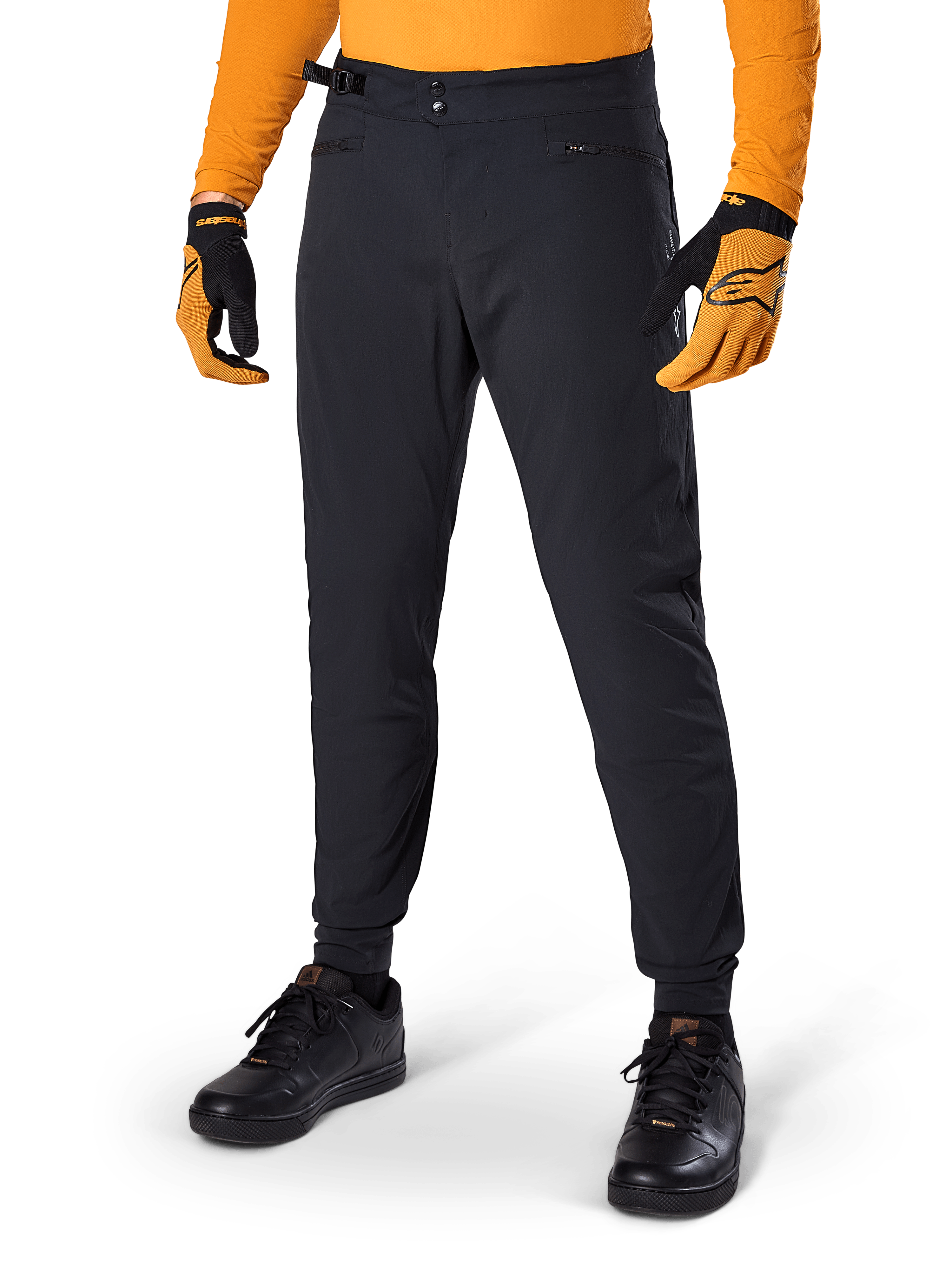 Alpinestars A-Dura Pants, mountainbikebroek, zwart, met zijsluitingen en zakken met rits, gedragen met oranje jersey en handschoenen, sportieve regular fit voor mountainbiken