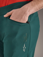 Alpinestars A-Dura Hose in Dark Pine Grün, Nahaufnahme einer Reißverschlusstasche mit Hand, weißes Alpinestars-Logo und Markenschriftzug am Oberschenkel, strapazierfähige MTB-Fahrradhose
