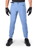 Alpinestars A-Dura Pants, MTB broek, Infinity Blue, lichtblauwe mountainbikebroek met dubbele drukknoopsluiting en zakken met ritssluiting, gedragen met zwarte handschoenen en zwarte schoenen, normale pasvorm met elastische manchetten