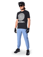 Alpinestars A-Dura broek, MTB-broek, Infinity Blue, gedragen met zwart grafisch T-shirt met wit spiraallogo, zwarte helm, zonnebril en zwarte handschoenen, professionele mountainbike-uitrusting