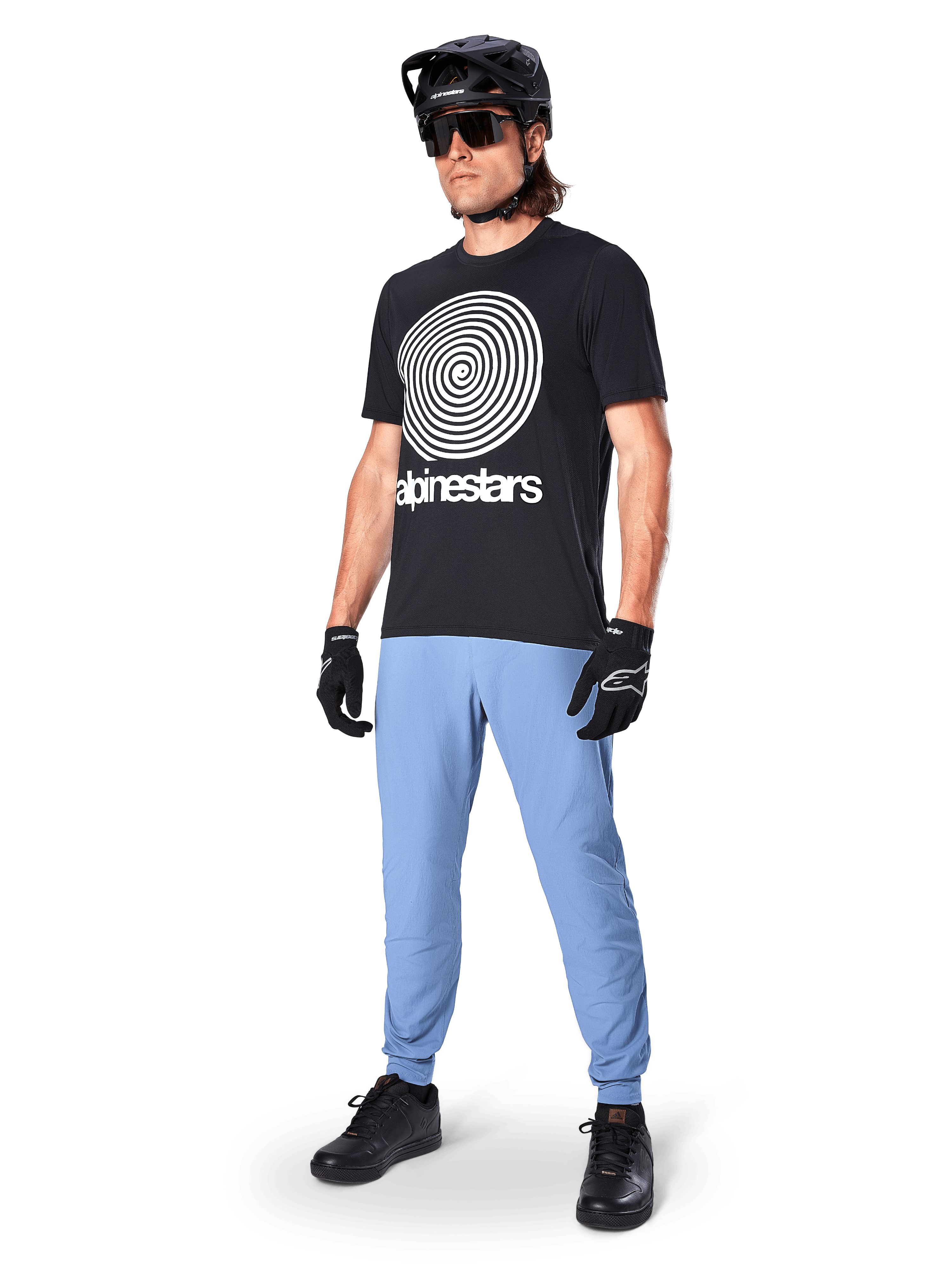 Alpinestars A-Dura broek, MTB-broek, Infinity Blue, gedragen met zwart grafisch T-shirt met wit spiraallogo, zwarte helm, zonnebril en zwarte handschoenen, professionele mountainbike-uitrusting