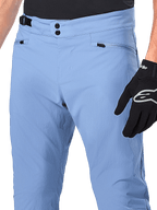 Alpinestars A-Dura Pants, MTB-fietsbroek, Infinity Blue, close-up van de taille met dubbele drukknoopsluiting en verstelbare tailleband aan de zijkant, zakken met rits, gedragen met zwarte Alpinestars handschoenen