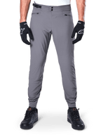 Alpinestars A-Dura Hose, dunkelgraue Mountainbike-Hose, Vorderansicht getragen mit schwarzen Handschuhen und schwarzen Sneakern, mit doppeltem Druckknopfverschluss, Reißverschlusstaschen und elastischen Bündchen, strapazierfähige Fahrradbekleidung für Trail-Riding