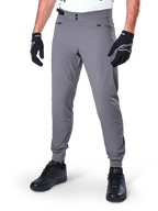 Alpinestars A-Dura Hose, dunkelgraue MTB-Hose, mit doppeltem Druckknopfverschluss und Reißverschlusstaschen, elastische Bündchen, getragen mit schwarzen Fahrradhandschuhen und schwarzen Sneakern