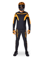 Alpinestars A-Supra Race Pants, pantalon de course VTT, noir et orange, porté par un pilote avec une tenue complète comprenant un maillot noir et orange, un casque orange et des gants assortis, avec logos étoiles orange sur les jambes