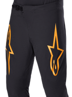 Pantalon Alpinestars A-Supra Race, pantalon de VTT noir avec grands logos étoiles orange, doté d'une fermeture à rochet à l'avant et de trous de ventilation perforés au laser, design technique axé sur la performance.