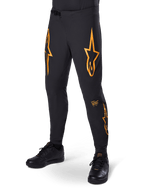 Alpinestars A-Supra Race Pants, noir avec motifs étoile orange, pantalon de course VTT doté de ventilations perforées au laser et d'une fermeture à rochet à la taille, coupe performance ajustée pour le cyclisme tout-terrain