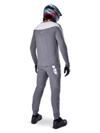 Alpinestars A-Supra Race Pants, gris foncé, cycliste de VTT vu de dos portant une tenue de course complète, maillot gris à manches longues, pantalon gris foncé avec logo blanc d'inspiration MX sur l'empiècement arrière, casque gris et bleu, chaussures noires, conçu pour la performance en VTT