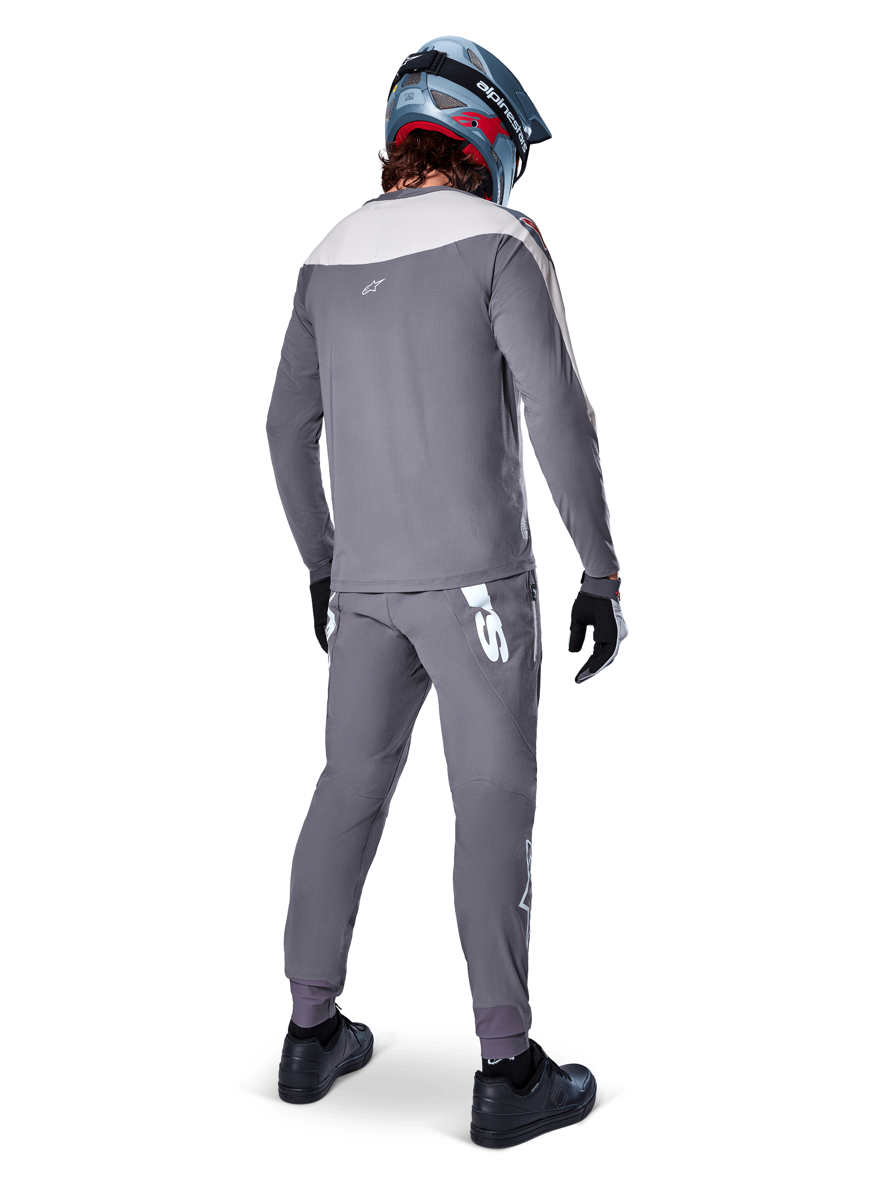 Alpinestars A-Supra Race Pants, gris foncé, cycliste de VTT vu de dos portant une tenue de course complète, maillot gris à manches longues, pantalon gris foncé avec logo blanc d'inspiration MX sur l'empiècement arrière, casque gris et bleu, chaussures noires, conçu pour la performance en VTT