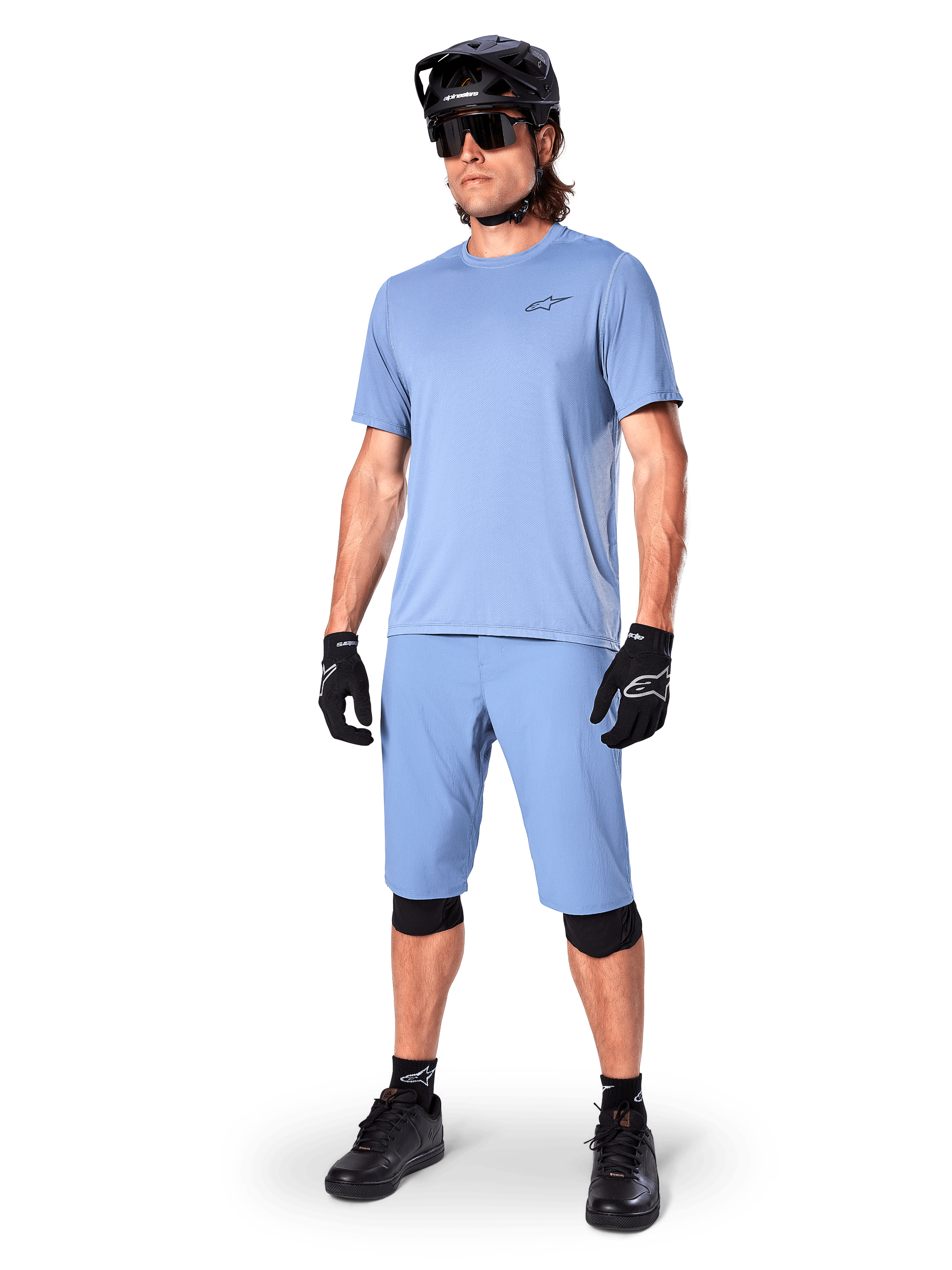 Modèle portant le short Alpinestars A-Dura en Infinity Blue, maillot à manches courtes bleu clair assorti, casque de VTT noir, lunettes de soleil et gants noirs, tenue de VTT complète pour le trail