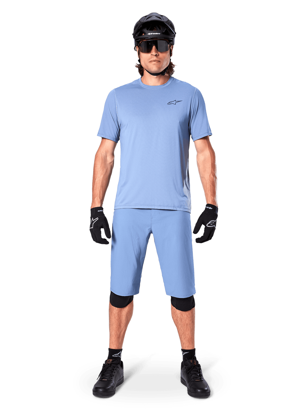 Modèle portant le short Alpinestars A-Dura en Infinity Blue, maillot bleu clair assorti, casque de VTT noir, lunettes de soleil noires, gants et genouillères noirs, tenue de VTT complète pour le trail