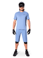Modèle portant le short Alpinestars A-Dura en Infinity Blue, maillot bleu clair assorti, casque de VTT noir, lunettes de soleil noires, gants et genouillères noirs, tenue de VTT complète pour le trail