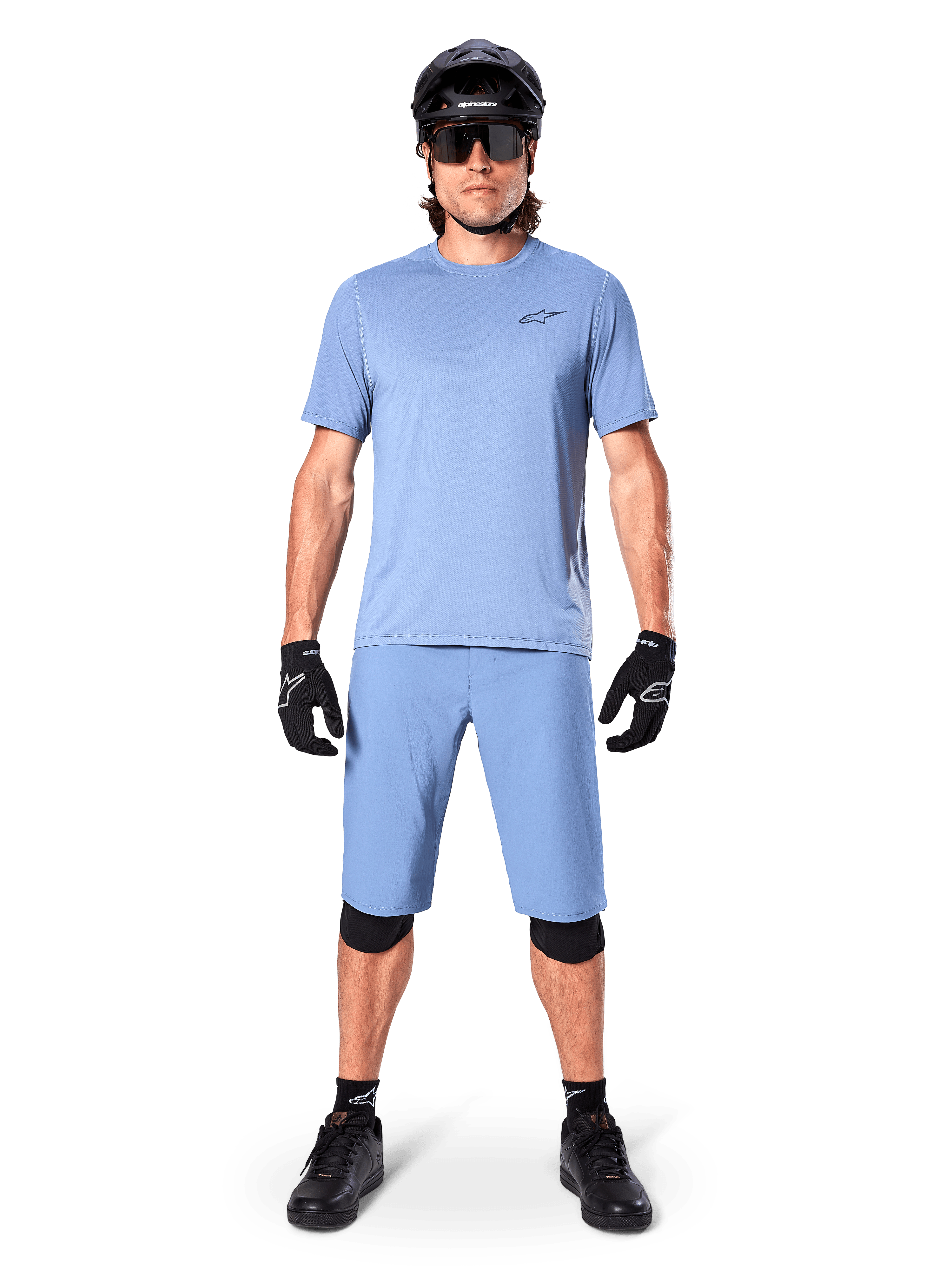 Modèle portant le short Alpinestars A-Dura en Infinity Blue, maillot bleu clair assorti, casque de VTT noir, lunettes de soleil noires, gants et genouillères noirs, tenue de VTT complète pour le trail
