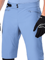 Short Alpinestars A-Dura, short de VTT bleu Infinity, gros plan sur la taille doté d'une double fermeture à pression, d'un ajusteur latéral et de poches zippées doublées en maille, porté avec un gant Alpinestars noir