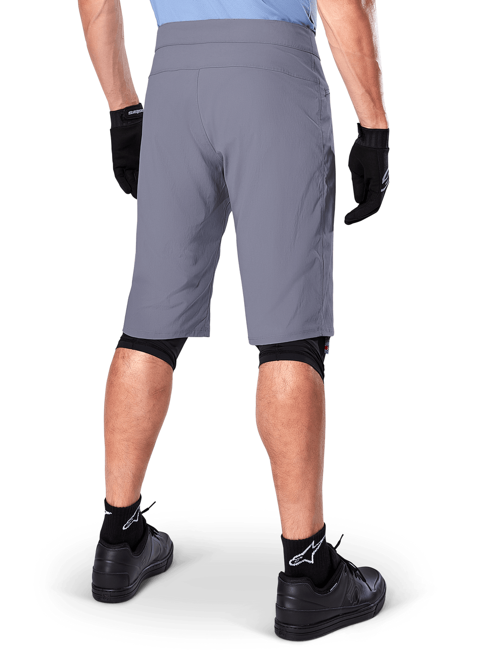 Short Alpinestars A-Dura, short de VTT gris foncé, vue arrière portée par un cycliste avec gants noirs, genouillères noires et chaussettes noires à logo Alpinestars, construction durable pour le cyclisme tout-terrain
