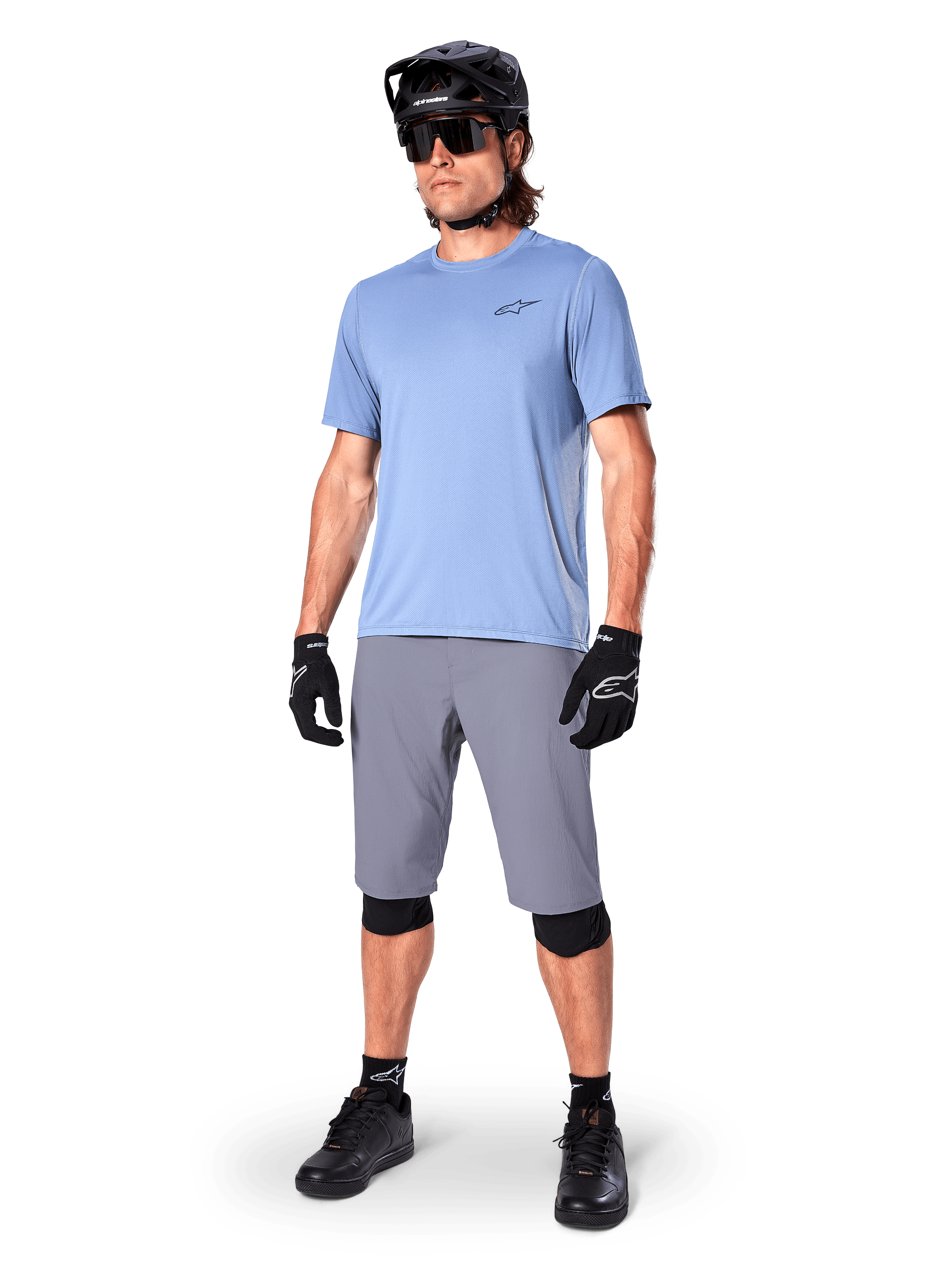 Short Alpinestars A-Dura, short de VTT, gris foncé, porté par un rider avec un maillot bleu clair, un casque de VTT noir, des gants noirs et des genouillères, tenue de VTT complète pour le trail et le tout-terrain