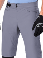 Alpinestars A-Dura Shorts, short de VTT, gris foncé, vue rapprochée de la taille montrant la double fermeture à pression, l'ajusteur latéral et les poches zippées, associé à des gants de cyclisme noirs, vêtement de VTT durable.