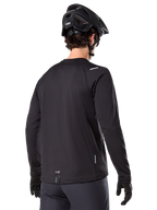 Maillot thermique Alpinestars A-Dura, maillot de VTT à manches longues, noir, vue de dos montrant la queue allongée, de petits détails réfléchissants et le marquage sur l'ourlet, porté avec un casque noir et des gants pour le cyclisme par temps froid