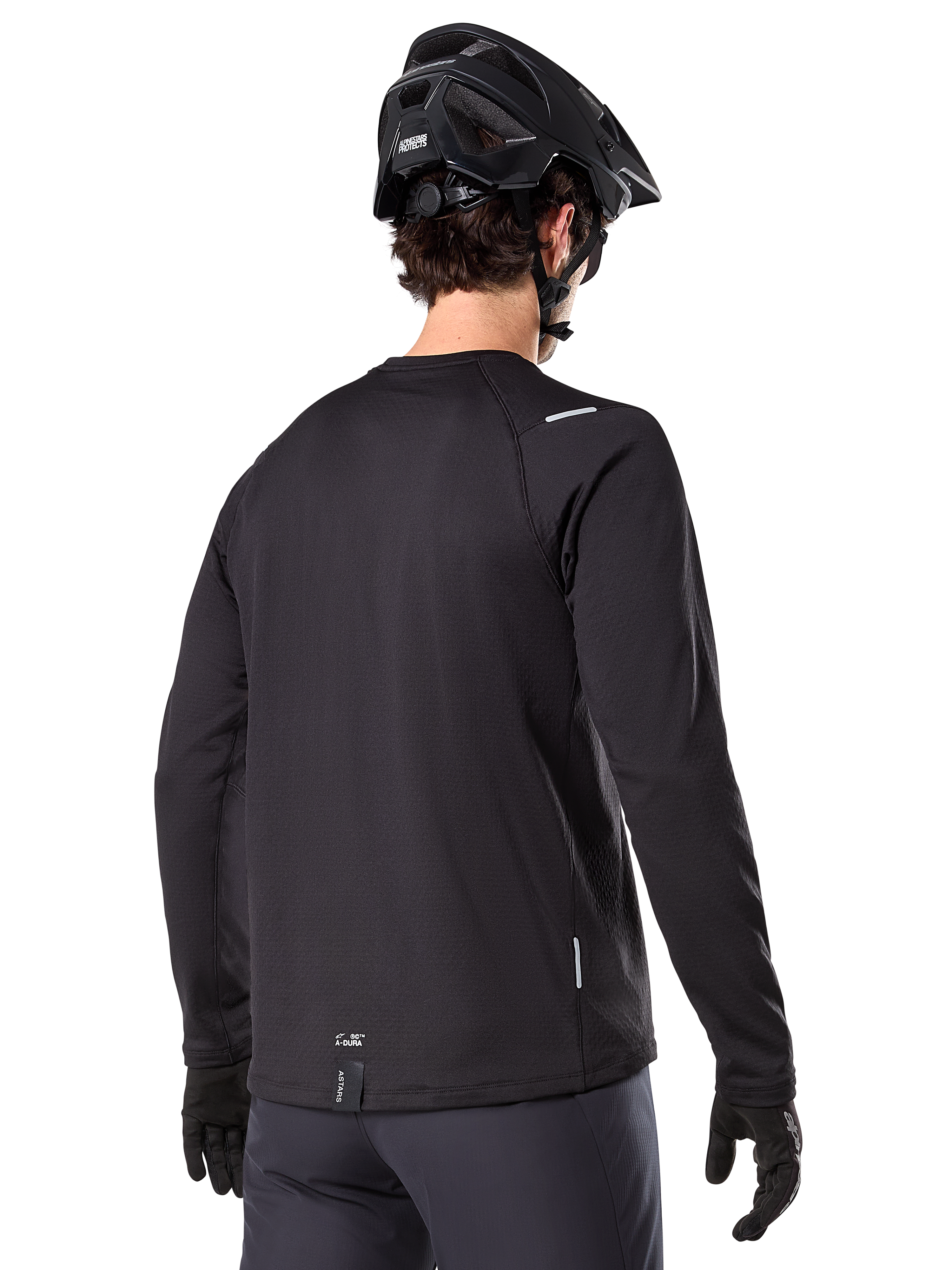 Maillot thermique Alpinestars A-Dura, maillot de VTT à manches longues, noir, vue de dos montrant la queue allongée, de petits détails réfléchissants et le marquage sur l'ourlet, porté avec un casque noir et des gants pour le cyclisme par temps froid