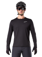 Maillot thermique Alpinestars A-Dura, maillot de VTT à manches longues noir, porté avec un casque noir et de larges lunettes de soleil, petit logo Alpinestars blanc sur la poitrine, coupe classique, équipement de cyclisme VTT
