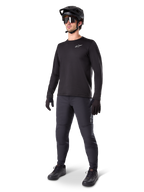 Modèle portant le maillot thermique Alpinestars A-Dura, maillot de VTT noir à manches longues, casque de VTT noir, lunettes de soleil et pantalon gris foncé, avec un petit logo blanc sur la poitrine, conception en polaire isolante pour rouler par temps froid