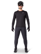 Alpinestars A-Dura Thermal Jersey, maillot de VTT à manches longues noir, porté avec un pantalon gris foncé, des gants noirs, un casque noir et des lunettes de soleil, logo Alpinestars blanc sur la poitrine, tenue coordonnée pour le VTT par temps froid