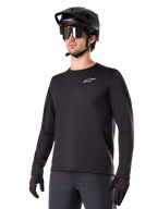 Alpinestars A-Dura Thermal Jersey, maillot de VTT à manches longues noir, logo blanc sur la poitrine, porté avec un casque et des gants noirs, design sportif et épuré pour le trail
