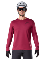 Maillot thermique Alpinestars A-Dura, maillot de VTT à manches longues pour homme, bordeaux, porté avec un casque gris et des lunettes de soleil noires, avec un petit logo étoile sur la poitrine, tissu polaire isolant pour le VTT par temps froid