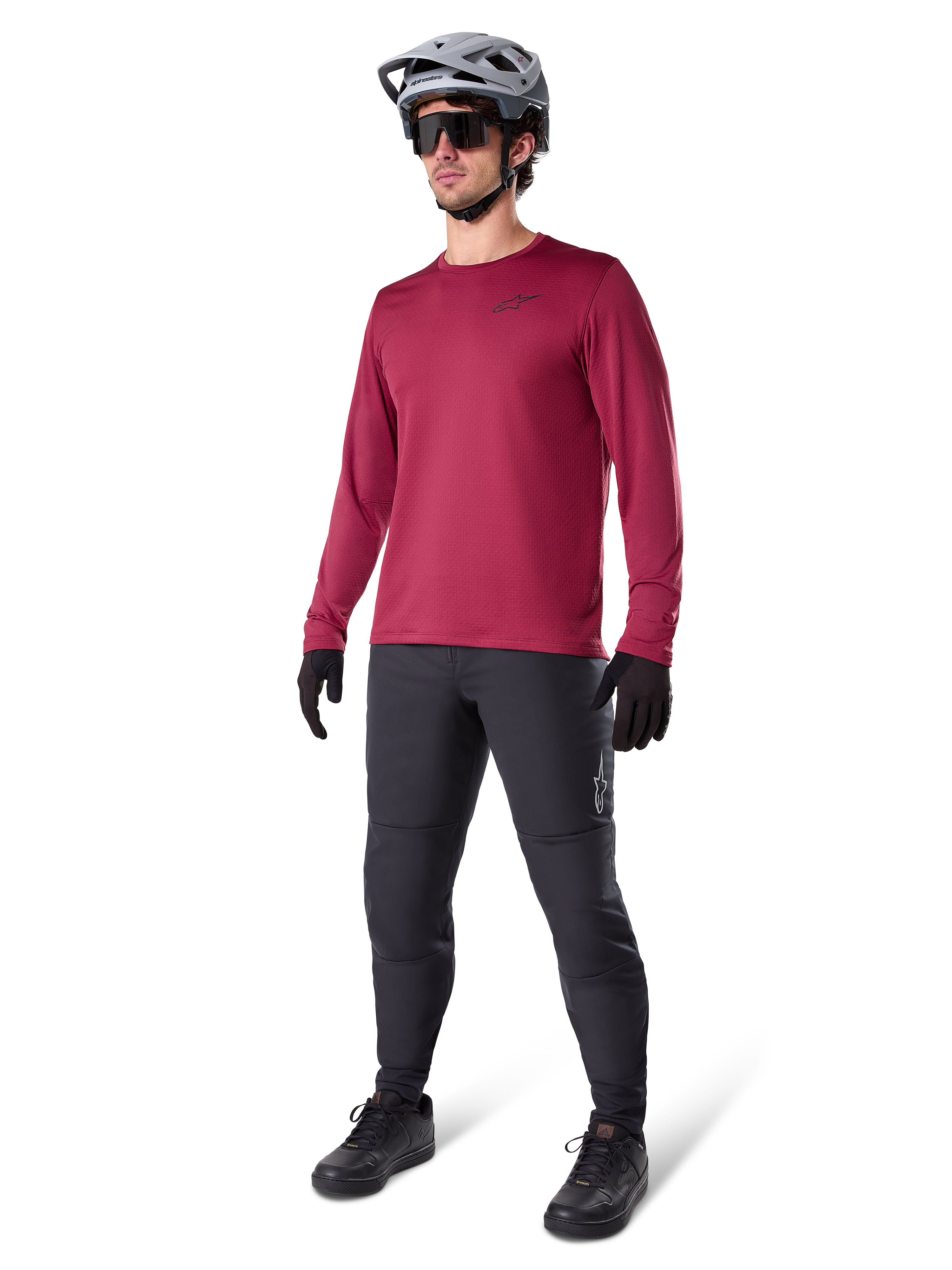 Maillot thermique Alpinestars A-Dura bordeaux, haut de cyclisme isolant à manches longues porté avec un pantalon de VTT gris foncé, des gants noirs et un casque gris, tenue complète de VTT pour temps froid, photo en studio
