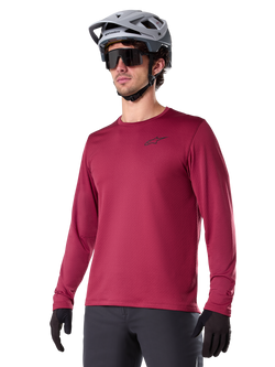 Alpinestars A-Dura Thermal Jersey, Langarm-Mountainbike-Trikot, Burgunderrot, mit isoliertem Fleece-Futter und kleinem schwarzem Brust-Logo, getragen mit einem grauen Helm, schwarzer Sonnenbrille und schwarzen Handschuhen, ideal für Radsport bei kaltem Wetter