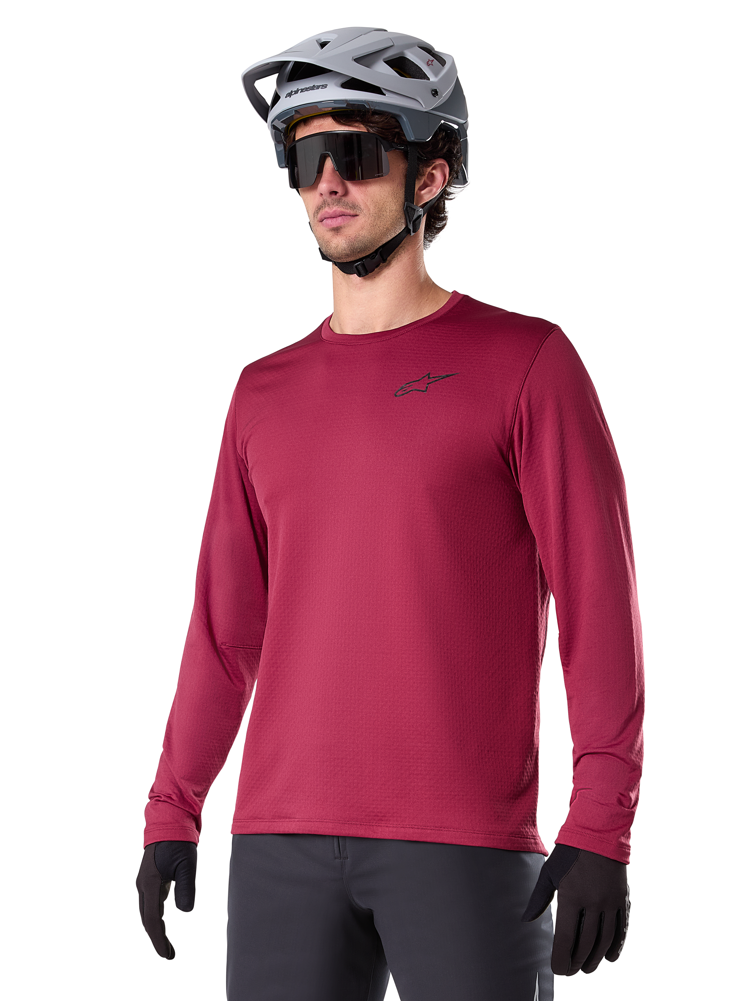 Maillot thermique Alpinestars A-Dura, maillot de VTT à manches longues, rouge bordeaux, avec doublure en polaire isolante et petit logo noir sur la poitrine, porté avec un casque gris, des lunettes de soleil noires et des gants noirs, conçu pour le cyclisme par temps froid