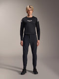 Alpinestars A-Aria Elite Pants, Black Titanium MTB-broek, gedragen door een mannelijk model met een bijpassende zwarte jersey met lange mouwen en sneakers, slim-fit prestatiegericht ontwerp met magnetische gespsluiting, technische mountainbikekleding