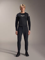 Alpinestars A-Aria Elite Pants, Black Titanium MTB-broek, gedragen door een mannelijk model met een bijpassende zwarte jersey met lange mouwen en sneakers, slim-fit prestatiegericht ontwerp met magnetische gespsluiting, technische mountainbikekleding