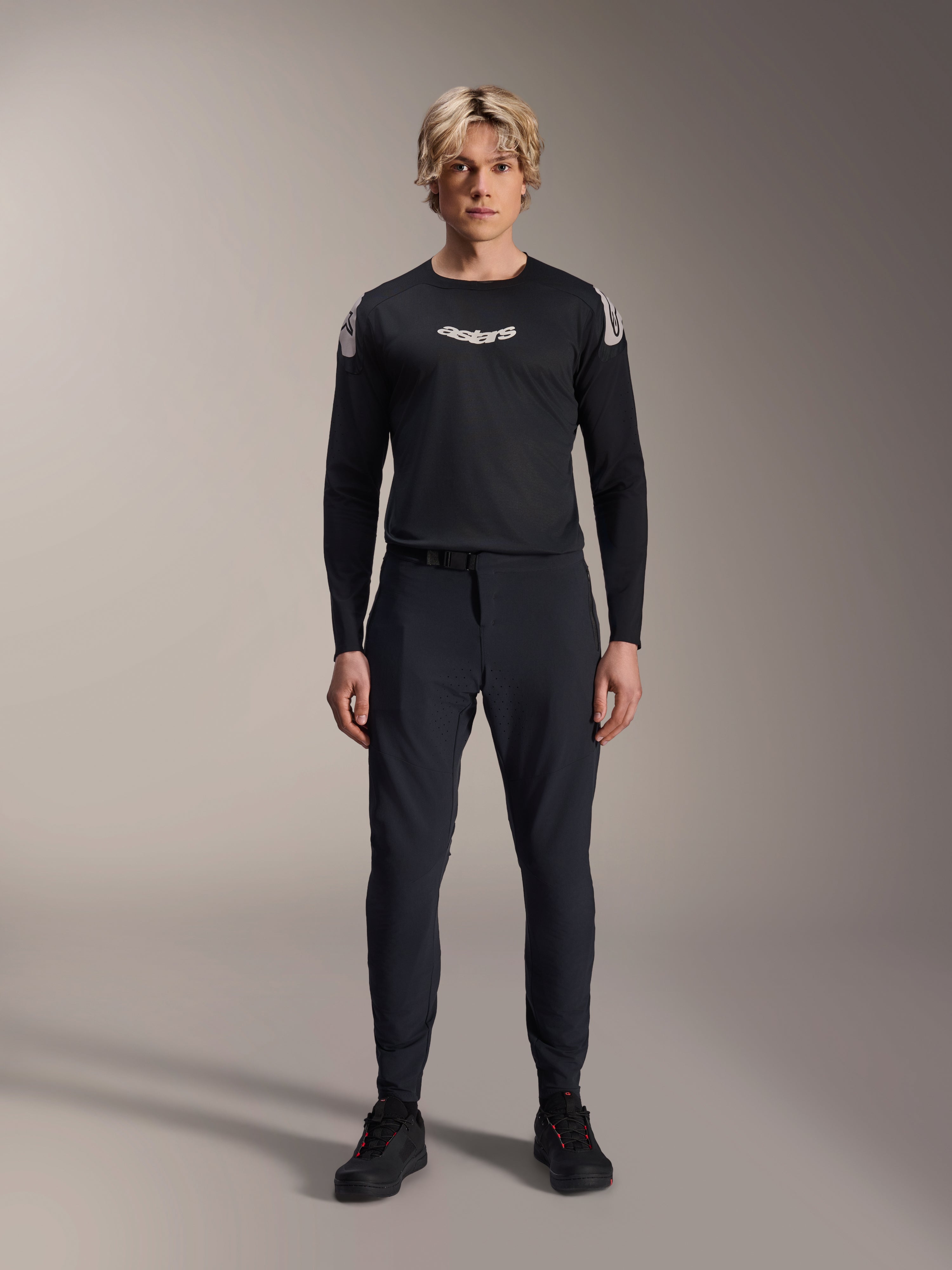 Alpinestars A-Aria Elite Hose, MTB-Hose in Black Titanium, getragen von einem männlichen Model mit einem passenden schwarzen Langarm-Trikot und Sneakern, Slim-Fit Performance-Design mit Magnetverschluss, technische Mountainbike-Bekleidung