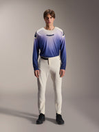 Alpinestars A-Aria Elite Pants, pantalon de VTT performance écru, pantalon de cyclisme blanc cassé avec panneaux sur les cuisses perforés au laser et boucle magnétique, porté avec un maillot à manches longues bleu dégradé et des chaussures noires, coupe performance pour le trail