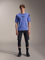Alpinestars A-Aria Elite Shorts, short de VTT, Noir Titane, porté avec un maillot bleu à manches courtes, des genouillères et des chaussures de vélo noires, photo de studio en pied, vêtements de VTT haute performance