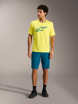 Gelbes Alpinestars A-Dura Ride SS Jersey und blaugrüne Shorts, Mountainbike-Performance-Outfit im Studio.