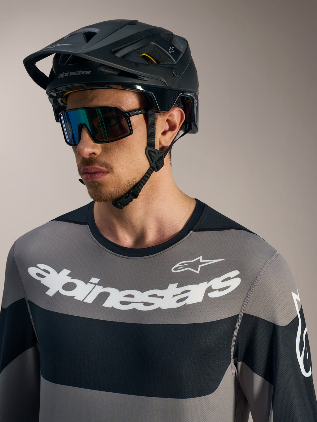 Alpinestars A-Dura Race jersey met lange mouwen in grijs, witte logo's, zwarte MTB-helm en sportieve zonnebril.