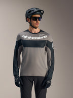 Grijs-zwarte A-Dura Race jersey met lange mouwen, wit Alpinestars-logo en MTB-helm voor trailrijden.