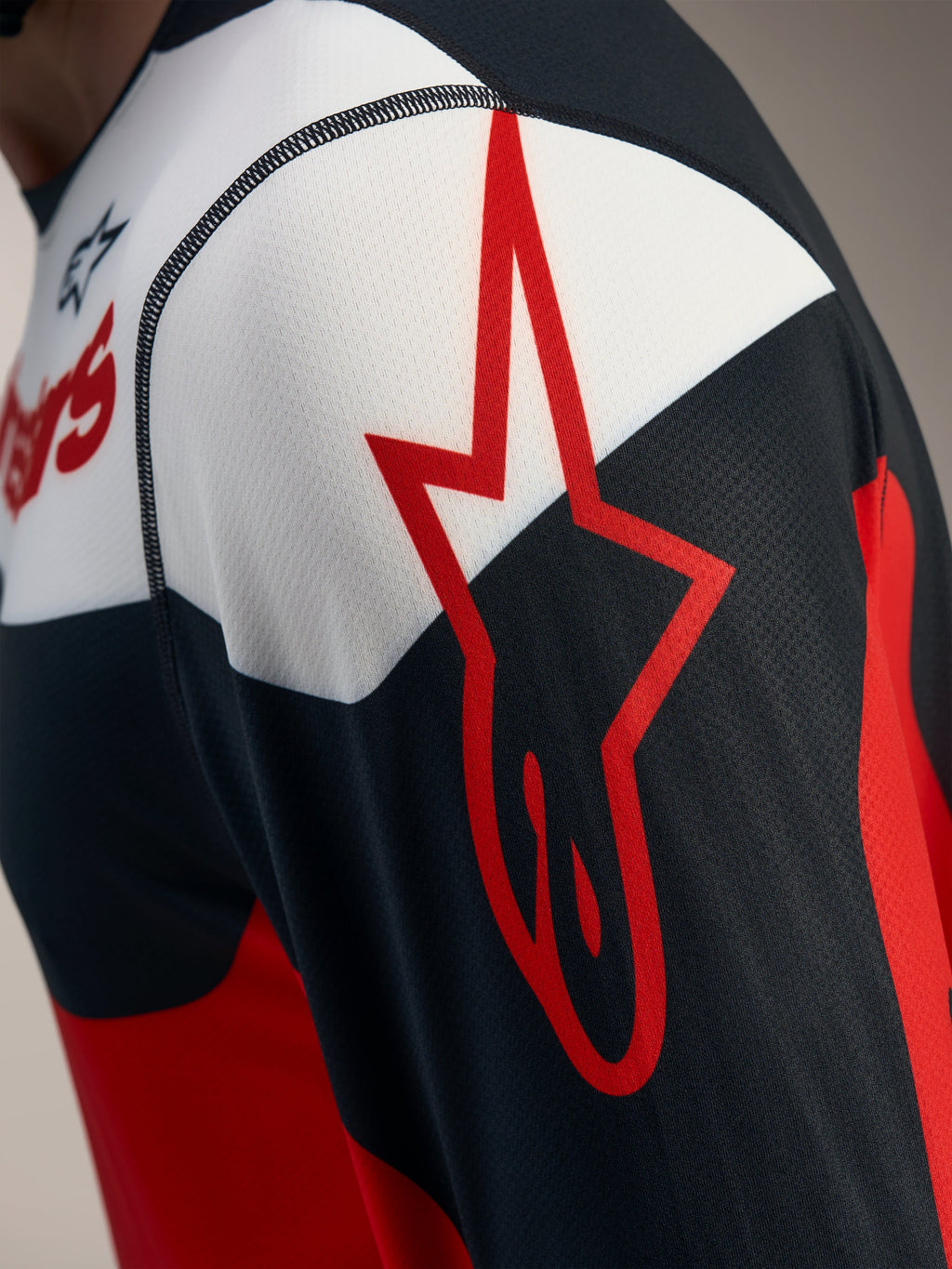 Detail van de rood-zwarte A-Dura Race trui met lange mouwen, Alpinestars-sterlogo op ademend jacquard mesh.