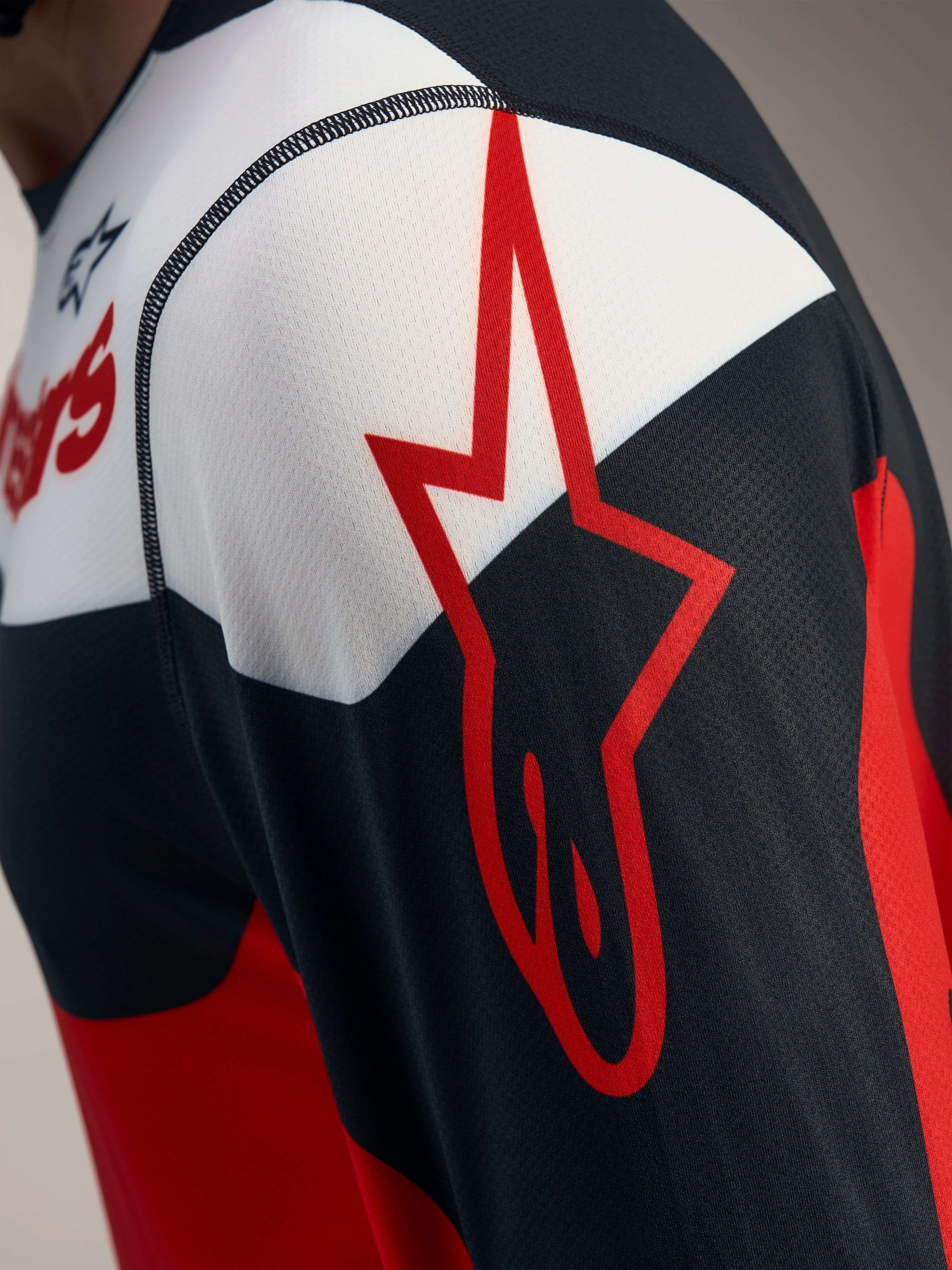 Detail van de rood-zwarte A-Dura Race trui met lange mouwen, Alpinestars-sterlogo op ademend jacquard mesh.