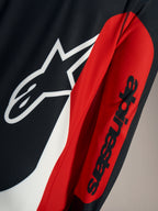 Detail van de A-Dura Race Trui met wit Astars-logo en zwart woordmerk op rode en zwarte technische mesh-stof.