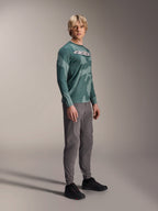 Alpinestars A-Dura Hollow Camo Langarm-Trikot, Silver Pine Camo, getragen von einem Model mit grauer Hose und schwarzen Schuhen, mit grünem Camouflage-Muster und markantem weißen ASTARS-Logo auf der Brust, Hochleistungs-MTB-Bekleidung