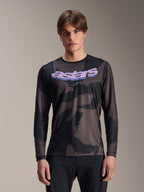 Alpinestars A-Dura Hollow Camo Long Sleeve Jersey, maillot de VTT, motif camouflage noir et gris, graphisme 'astars' violet sur la poitrine, porté par un mannequin avec un pantalon noir, design technique décontracté