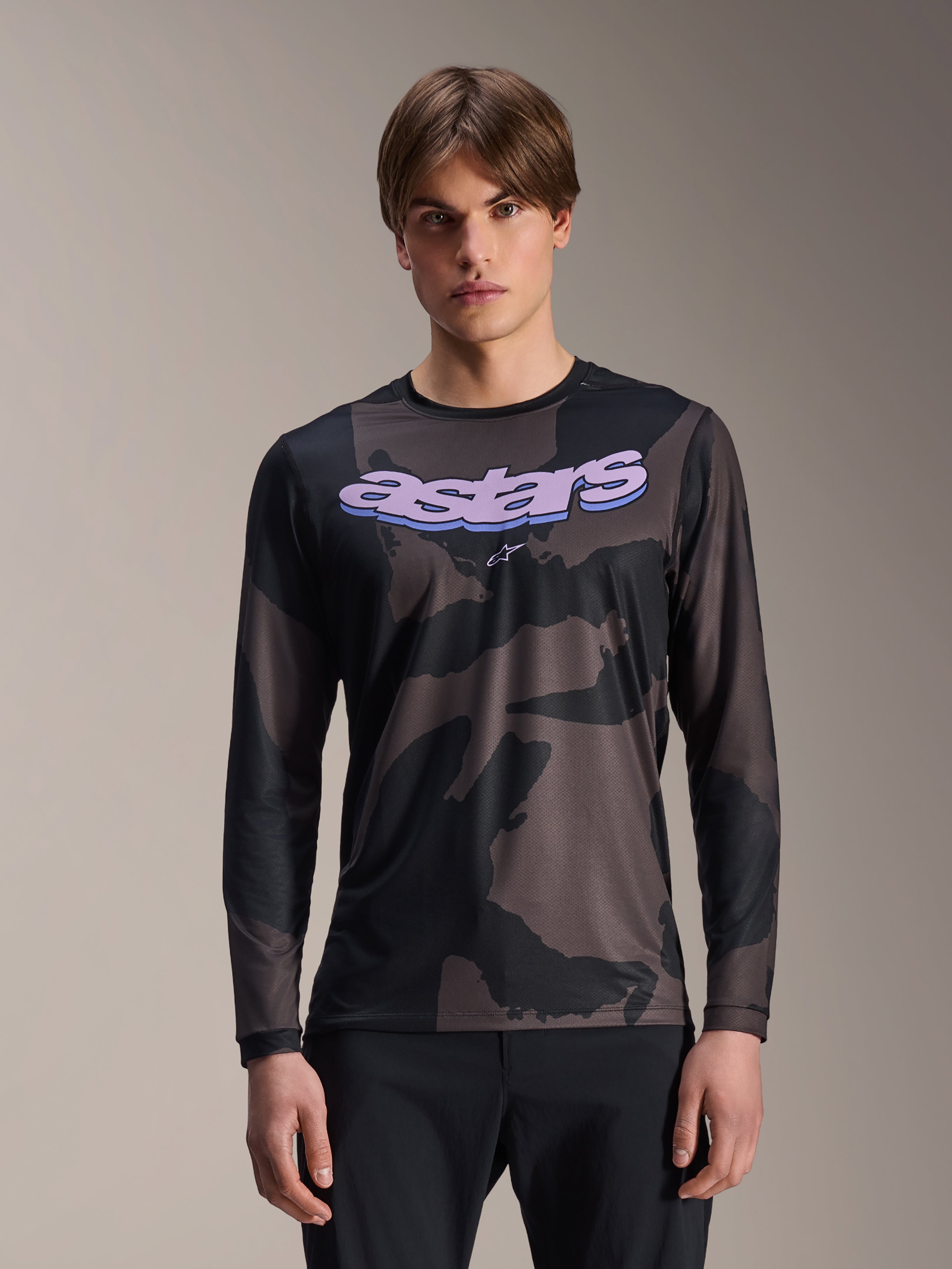 Alpinestars A-Dura Hollow Camo Langarmtrikot, MTB-Mountainbike-Trikot, schwarz-graues Camouflage-Muster, lila „astars“-Grafik auf der Brust, getragen von einem Model mit schwarzer Hose, lässiges Performance-Design