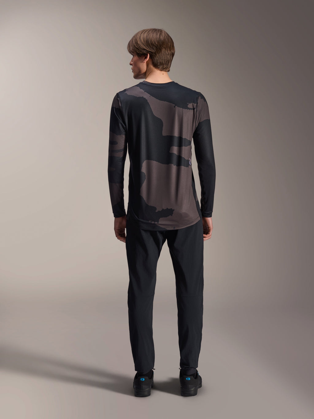 Maillot à manches longues Alpinestars A-Dura Hollow Camo, Camo noir, vue de dos porté avec un pantalon noir, présentant un motif camouflage sombre et un pan arrière allongé pour une couverture optimale en VTT.