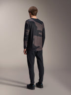Maillot à manches longues Alpinestars A-Dura Hollow Camo, Black Camo, vue arrière du mannequin, maillot technique de VTT avec pan arrière allongé, associé à un pantalon noir et des chaussures de cyclisme, équipement de performance tout-terrain décontracté