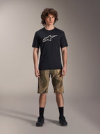 Alpinestars A-Dura Astar Kurzarm-Trikot, Schwarz mit großem weißem Astars-Logo auf der Brust, getragen von einem Model mit Camouflage-MTB-Shorts und schwarzen Radschuhen, lässige Mountainbike-Bekleidung.