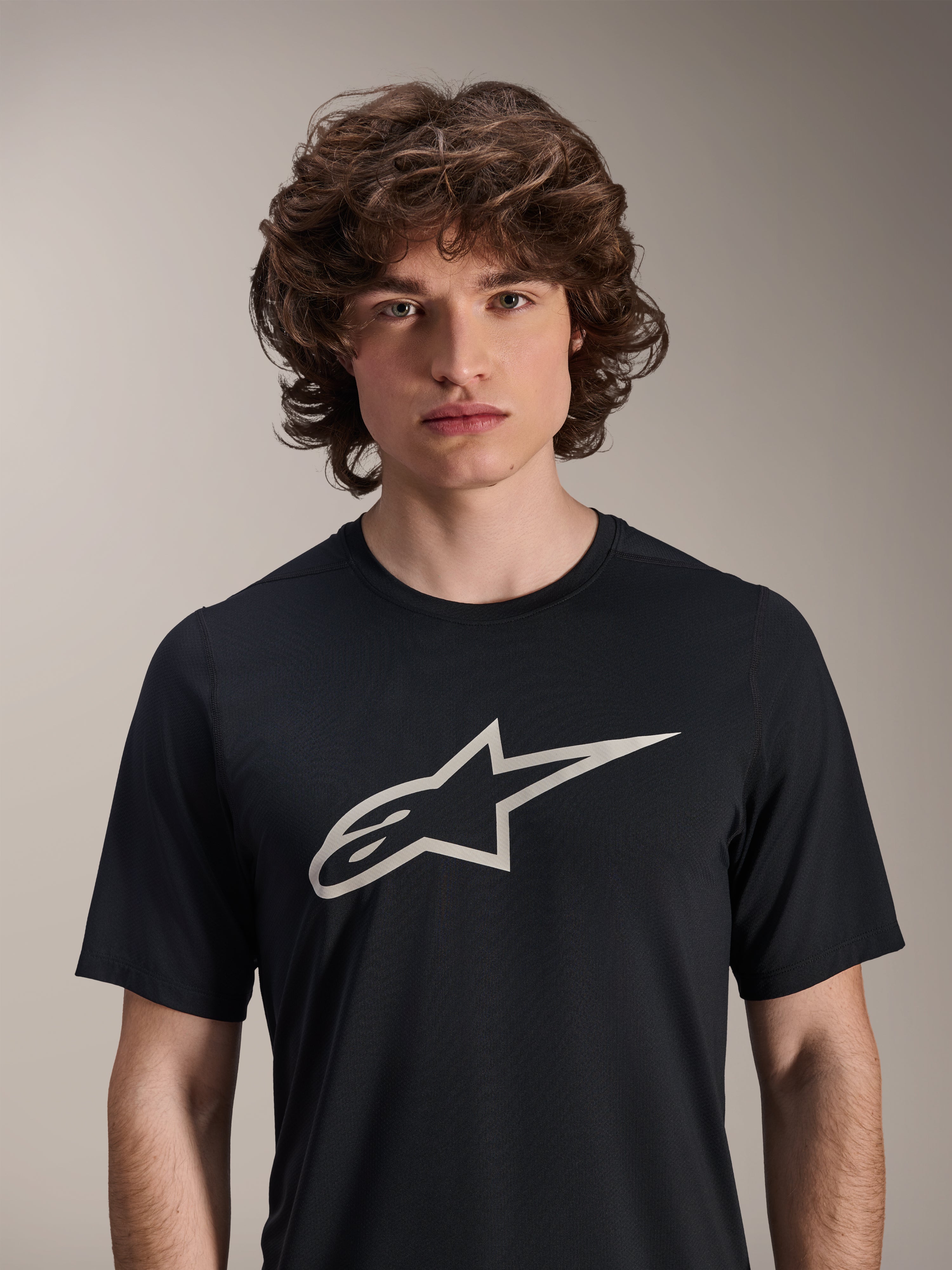 Alpinestars A-Dura Astar Kurzarm-Trikot, Schwarz, mit großem weißem Astar-Logo auf der Brust, getragen von einem männlichen Model, lässige Mountainbike-Performance-Bekleidung