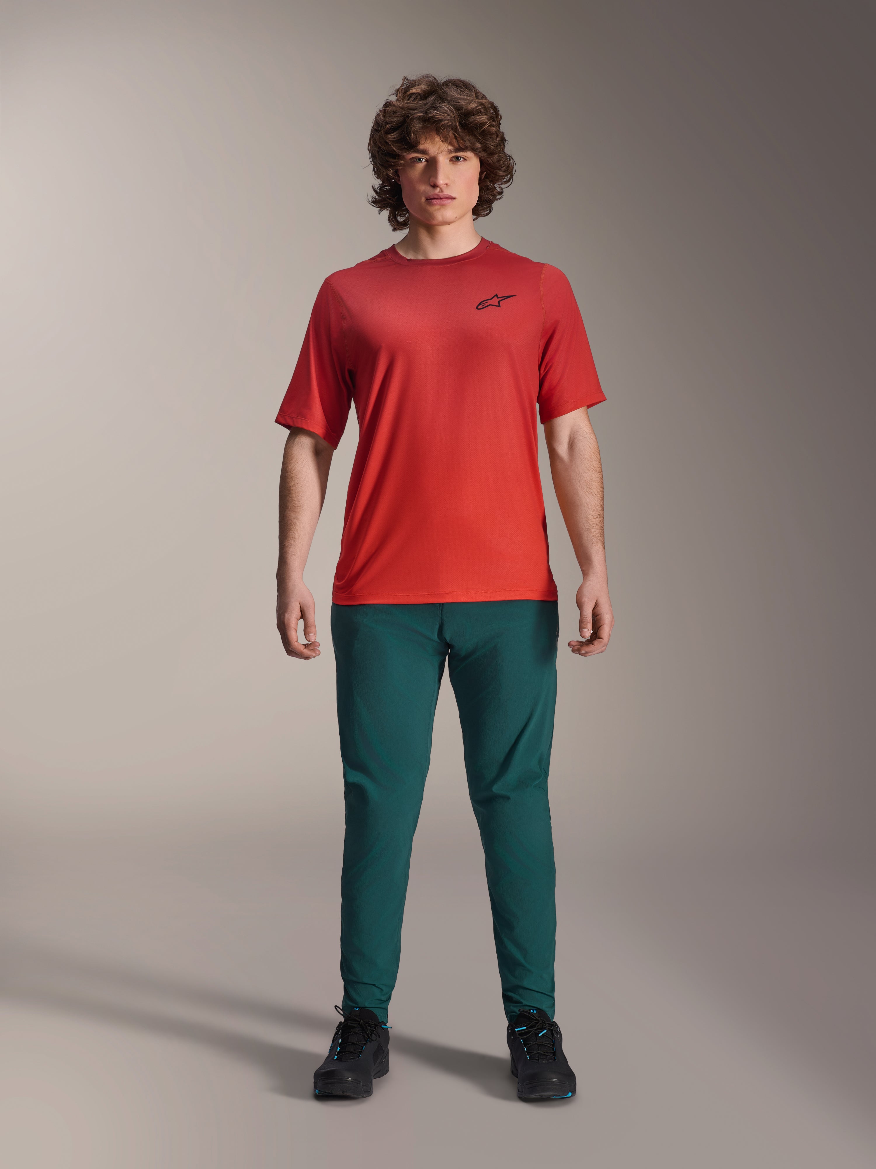 Alpinestars A-Dura Pants in Dark Pine groen gecombineerd met een rood A-Dura Rise Jersey met korte mouwen, model poserend in volledige mountainbike-outfit, casual performance pasvorm, duurzame MTB-kleding